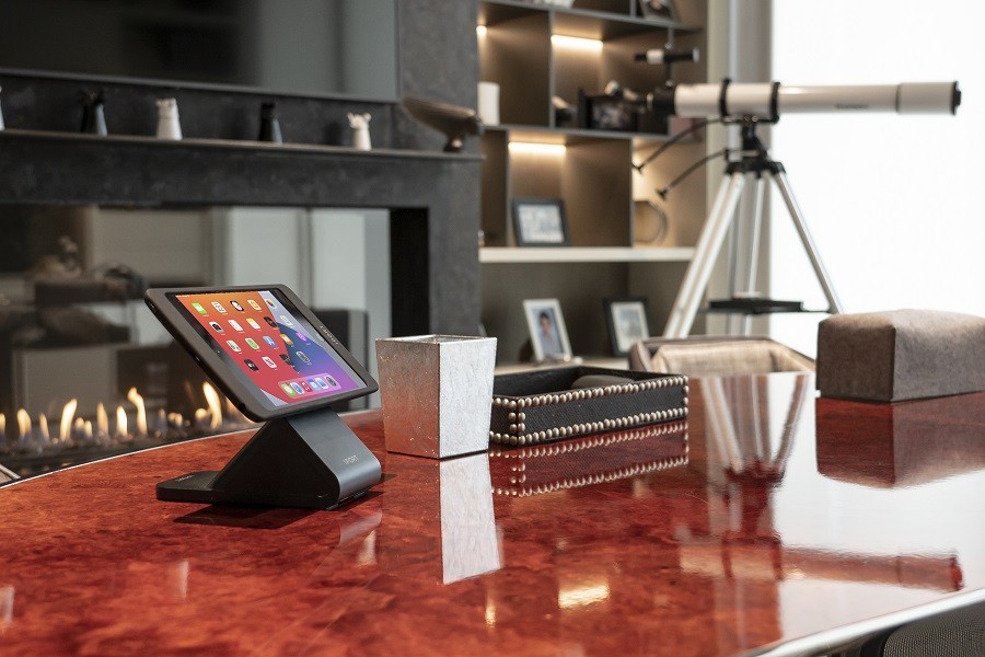 A Control4 touchscreen sits atop a rosewood desk with a modern gas fireplace, telescope, and minimalist decor. 