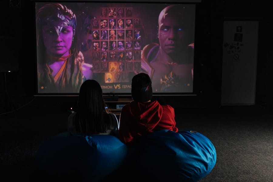 Two people sitting in bean bags in a home theater playing video games on a console.