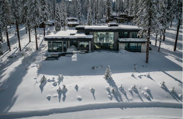 Modern house surrounded by snow and pine trees aerial front view