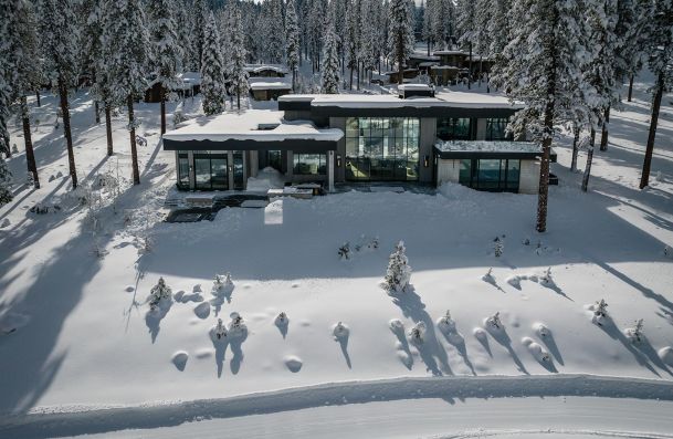 Modern house surrounded by snow and pine trees aerial front view