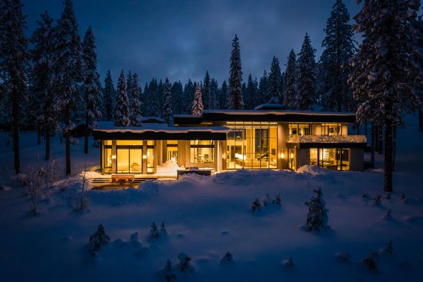 Modern house lighting at night surrounded by snow and pine trees back view
